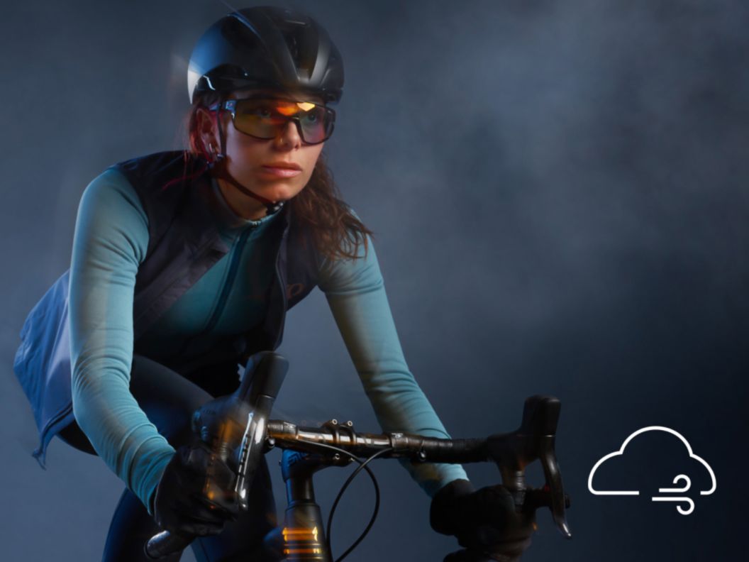   A glowy and slightly motion-blurred image of a road rider in lightweight thermal apparel with their vest open while pedaling in the drops. 